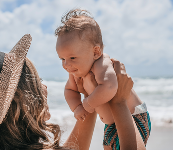 a mother holding her baby on the beach during the summer