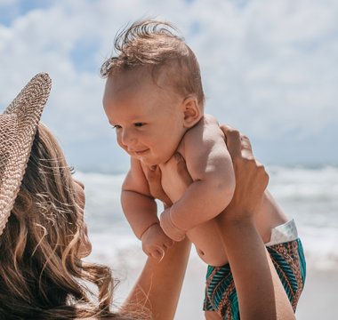 a mother holding her baby on the beach during the summer