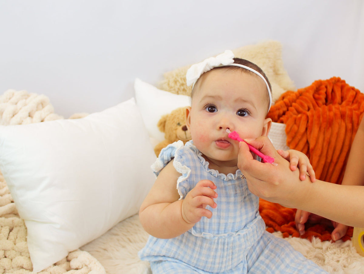 Parent gently cleaning a smiling baby's nose with an oogiebear booger picker
